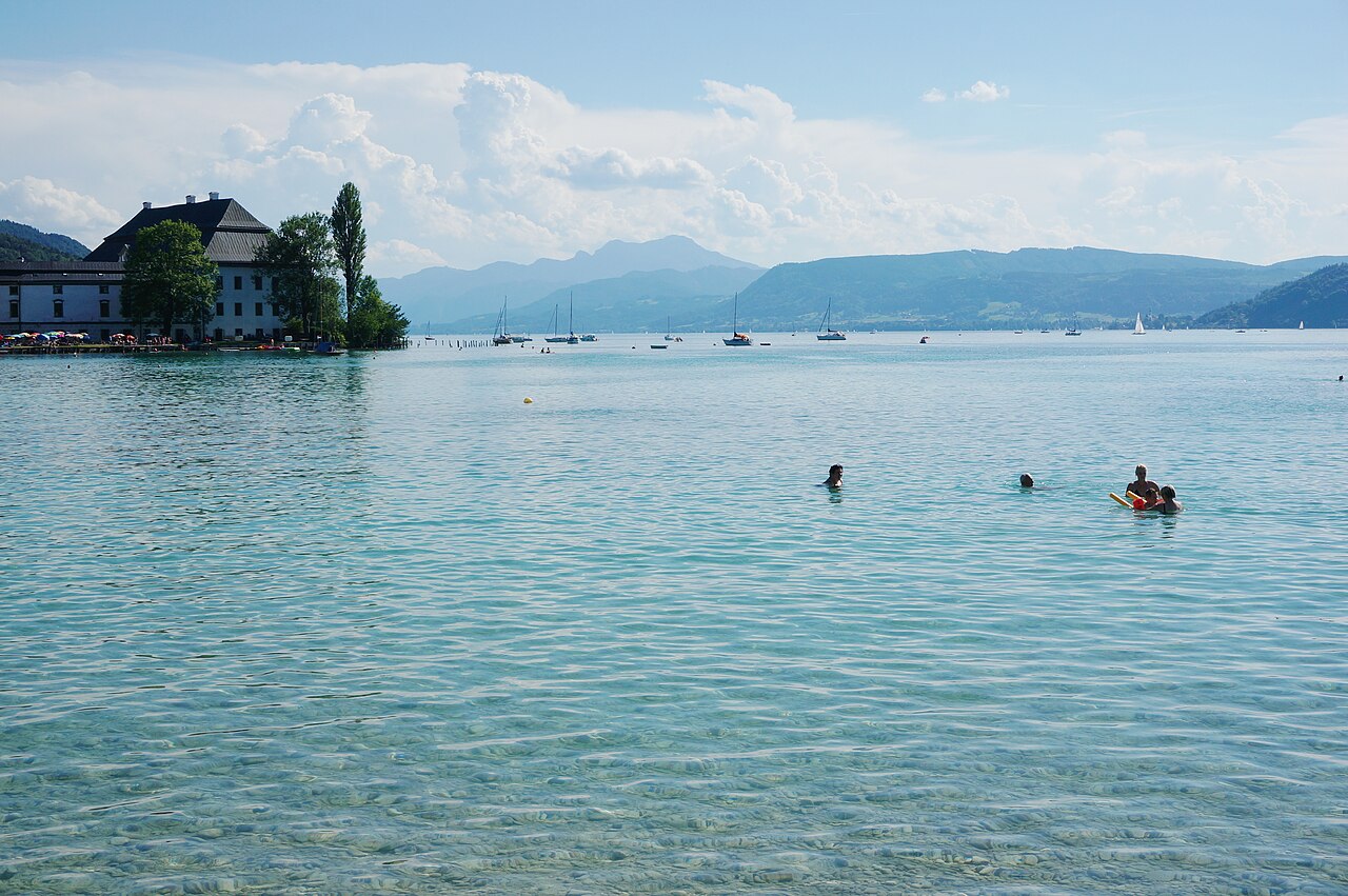 Klares Wasser am Attersee mit Schloss Kammer, Badegästen und Bergkulisse